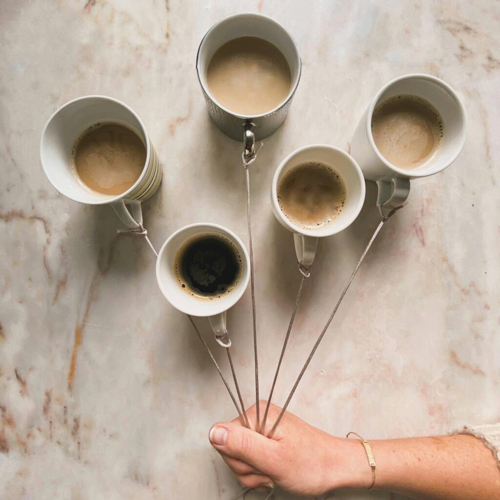 From above of crop unrecognizable female holding ropes tied to mugs with various types of Italian coffee on marble table